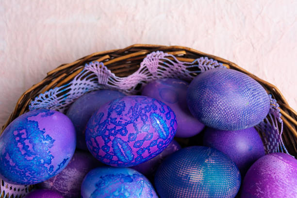 Blue-purple Easter eggs with a lace look in a wooden bowl on a pastel background.