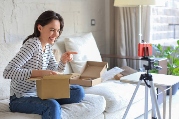 istock Young beautiful female blogger recording video while unpacking parcel at home. 1390604991