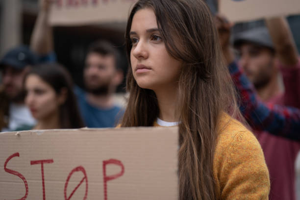 Crowd of young people protesting - focus on a young woman with a placard saying "Stop" - generic illustration for protest marches for human rights concept stock photo