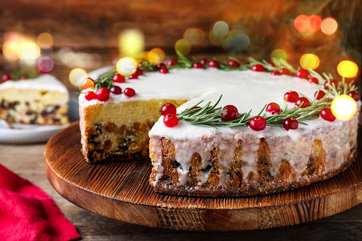 Traditional Christmas cake decorated with rosemary and cranberries on table, closeup. Bokeh effect