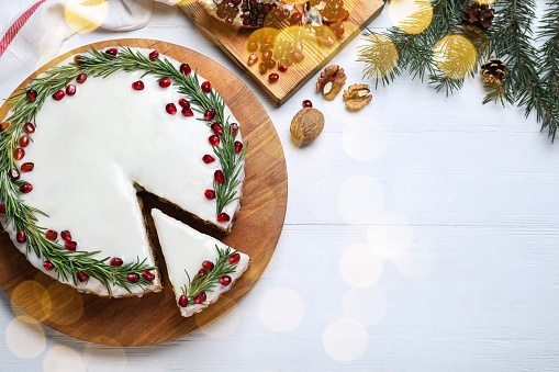 Flat lay composition with traditional Christmas cake on white wooden table, space for text. Bokeh effect