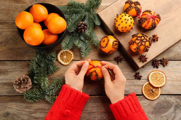 Woman decorating fresh tangerine with red ribbon at wooden table, top view. Making Christmas pomander balls Woman decorating fresh tangerine with red ribbon at wooden table, top view. Making Christmas pomander balls scent container stock pictures, royalty-free photos & images