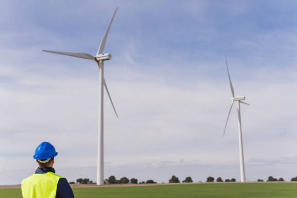 pessoa irreconhecível olhando para geradores elétricos em um parque eólico. engenheiro em roupas de trabalho e equipamentos de proteç�ão individual que procuram instalações energéticas limpas e não poluentes. - fuel and power generation nonpolluting wind turbine - fotografias e filmes do acervo