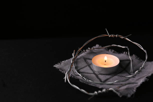 istock Fabric with star of David, barbed wire and burning candle on black background, space for text. Holocaust memory day 1390606368