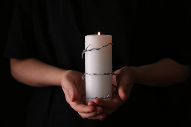 woman holding candle with barbed wire on black background, closeup. holocaust memory day - holocausto imagens e fotografias de stock