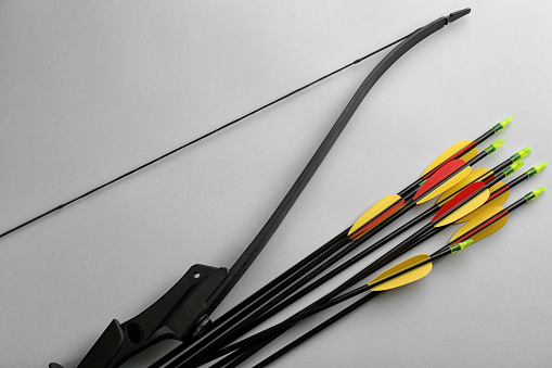 Black bow and set of arrows on light grey background, flat lay. Archery sports equipment