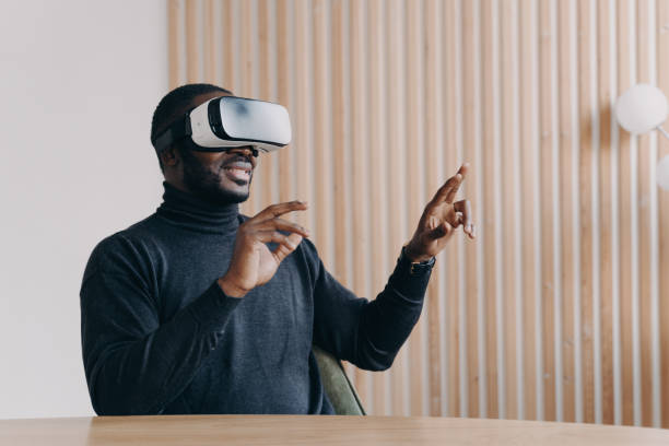 istock Young joyful African man office worker in VR headset glasses playing favorite 3D game 1390612080