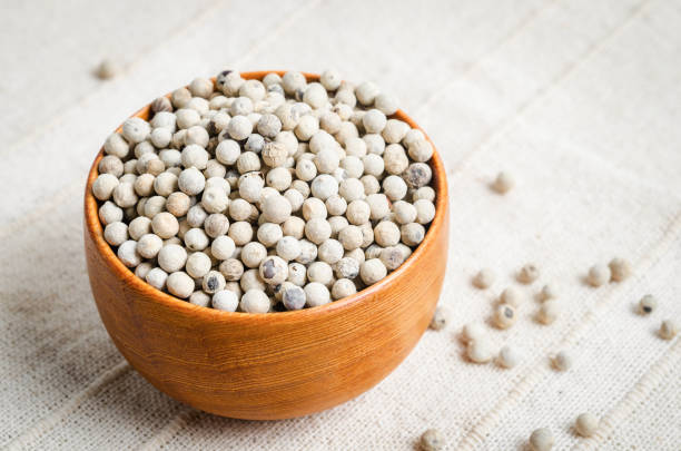 White pepper seeds (peppercorn) in wooden bowl on tablecloth background.