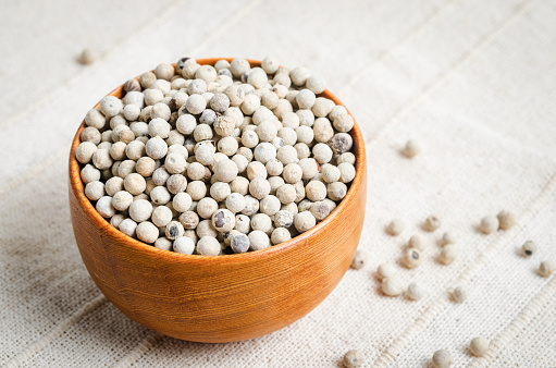 The White pepper seeds (peppercorn) in wooden bowl on tablecloth background.