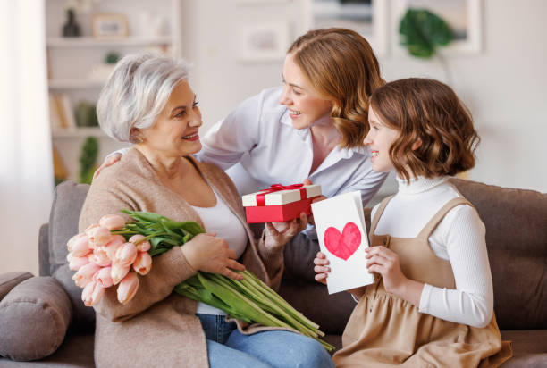 happy international mother's day.smiling  daughter and granddaughter giving flowers  and gift to grandmother   celebrate spring holiday women's day at home - grandmother giving gift child imagens e fotografias de stock