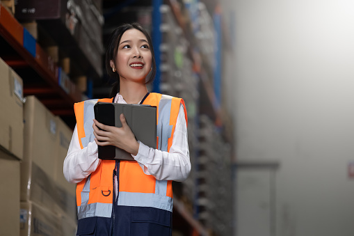 Professional beautiful asian woman worker checks stock and inventory with digital tablet computer in the retail warehouse full of shelves with goods. Working in logistics, Distribution center.