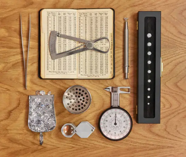 Square photograph showing diamond instruments and tools with loose diamonds on brown wood background.