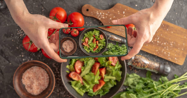 istock Women's hands are holding a mobile phone over a beautiful appetizing vegetable salad to take a photo 1390624092