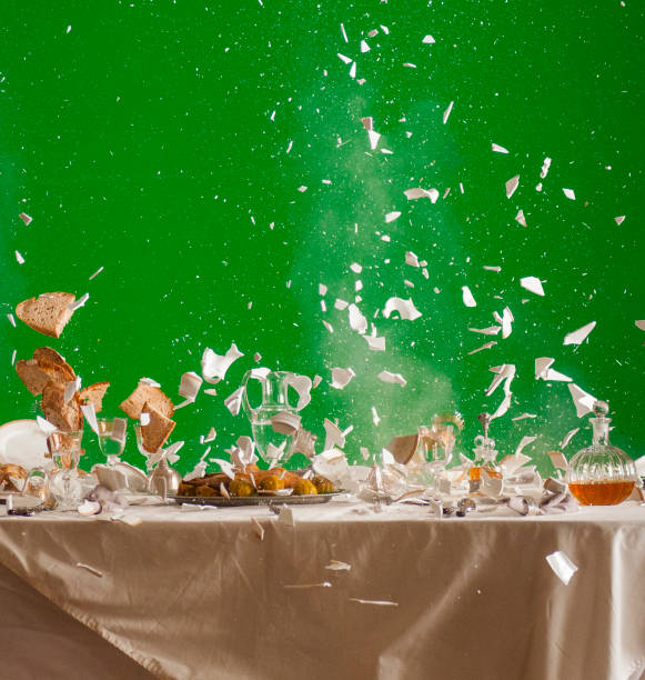fragments of dishes and bread flying over the table during an explosion on a green background stock photo