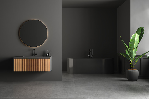Dark bathroom interior with concrete floor, black bathtub, and oval mirror standing on black wall. Minimalist black bathroom with modern furniture. 3D Rendering