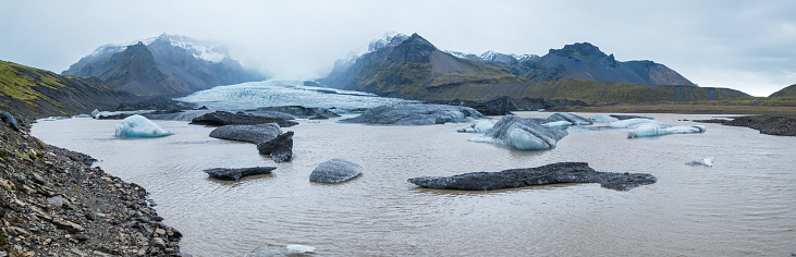 Glacier tongue slides from the Vatnajökull icecap or Vatna Glacier near subglacial Öræfajökull volcano, Iceland. Glacial lagoon with ice blocks and surrounding mountains.