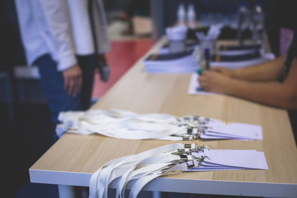 Process of checking in on a conference congress forum event, registration desk table, visitors and attendees receiving a name badge and entrance wristband bracelet and register electronic ticket stock photo