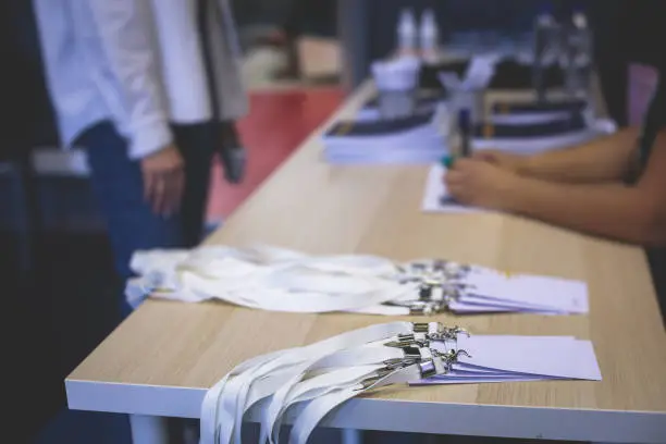 Photo of Process of checking in on a conference congress forum event, registration desk table, visitors and attendees receiving a name badge and entrance wristband bracelet and register electronic ticket