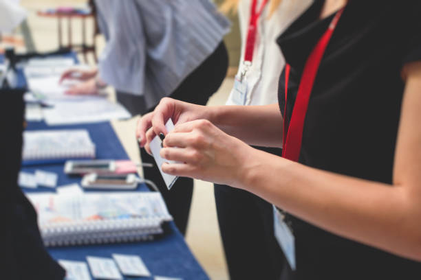 istock Process of checking in on a conference congress forum event, registration desk table, visitors and attendees receiving a name badge and entrance wristband bracelet and register electronic ticket 1390643454