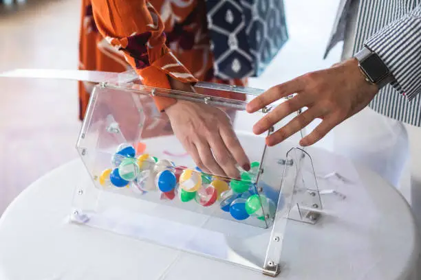 Photo of Process of prize drawings, extracting a winning numbers of lottery machine, raffle drum with bingo balls and winning tickets on event with a host and hands on lottery machine