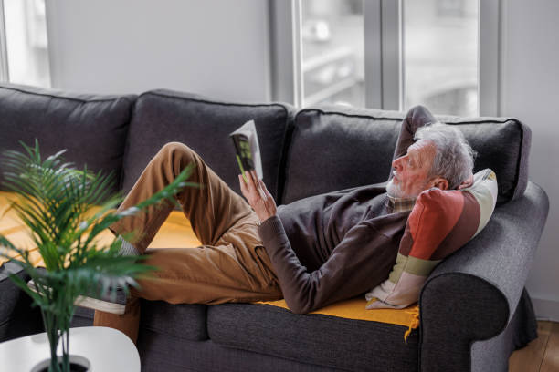 istock Image of a concentrated handsome senior man lying on sofa at home which reading book. 1390650725