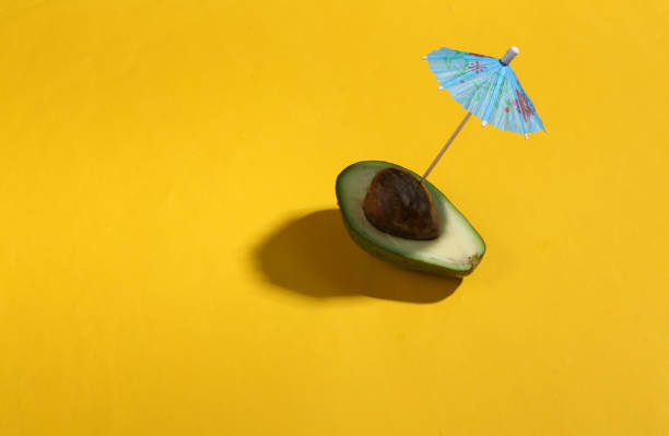 istock Minimal summer still life. Half an avocado with an umbrella on a bright yellow background. Creative layout 1390653384