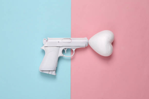 istock White gun with heart on blue-pink pastel background. Minimal, creative layout, love concept, top view 1390653645