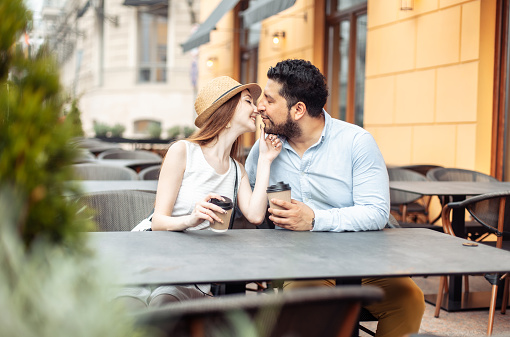 International couple in love drinking coffee while sitting at table in outdoor cafe