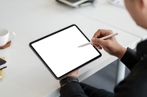 Asian male drawing on a white blank screen computer tablet with pen stylus.