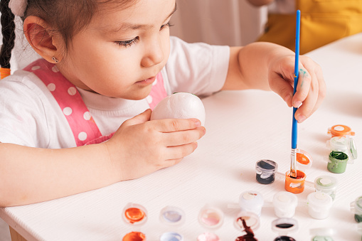 Child paints eggs with different colors.