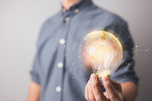 Businessman hand holds a lit light bulb with a network connecting line, representing the concepts of idea, innovation, and inspiration. Lights glow and glitter, you may create a unique concept.