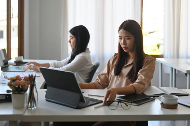 istock two beautiful serious Asian employees working on a tablet notebook in the office separately. 1390659453