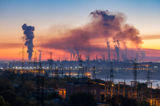 paesaggio industriale di tubi di impianti che producono fumo tossico con inquinamento atmosferico nel cielo al tramonto, diga idroelettrica e torri ad alta tensione, zaporizhzhia, ucraina - power station factory industry pollution foto e immagini stock