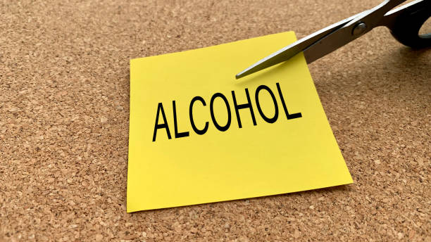 istock Scissors that cut yellow notepad with alcohol text on a wooden desk background. Spending concept 1390661588
