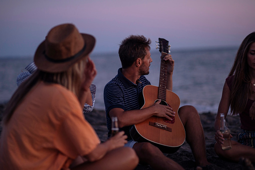 Mid adult man playing acoustic guitar to his friends on the beach