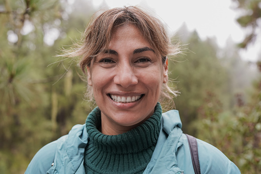 Mature latin woman smiling on camera during trekking day in nature forest
