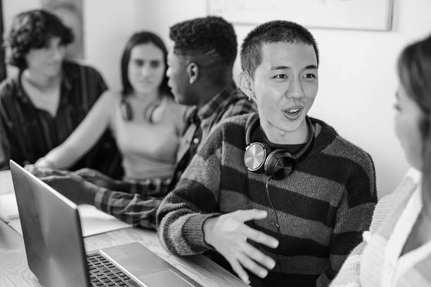 Young multiracial students learing together inside classroom using computer laptop and books