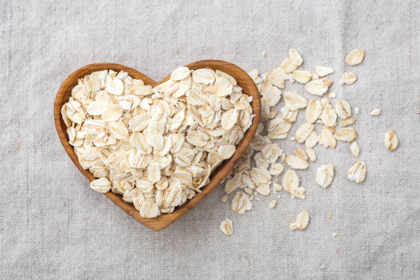 flocons d’avoine roulés dans un bol en bois de cœur sur tissu de lin - oatmeal oat heart shape rolled oats photos et images de collection