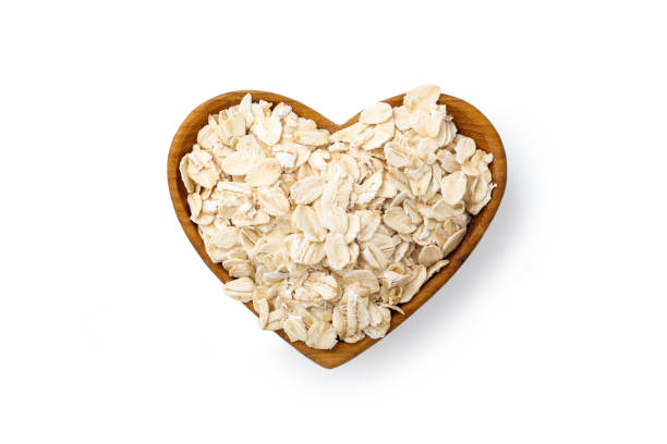 flocon d’avoine roulé dans un bol en bois de cœur isolé sur blanc - oatmeal oat heart shape rolled oats photos et images de collection