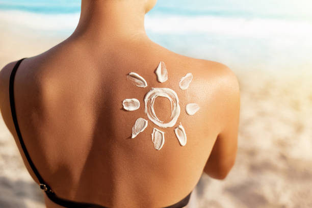 Sun Protection.Sun Cream. Woman Applying Sun Cream on Tanned  Shoulder In Form Of The Sun. Skin and Body Care. Girl Using Sunscreen to Skin. stock photo