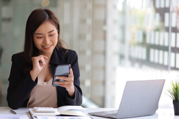 istock Happy businesswoman using mobile phone while working at office with laptop and messaging with smartphone. 1390671216