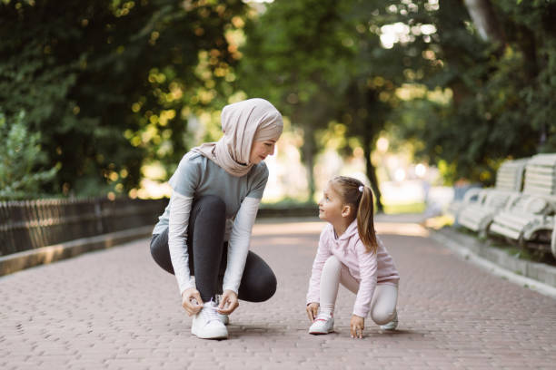 mutter im hijab, die mit ihrer tochter schnürsenkel zusammenhält, bereit, sich im freien zu betätigen - shoe women adult baby stock-fotos und bilder