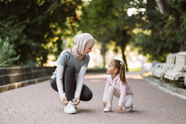 mother in hijab, tying laces together with her daughter, ready to do physical activity outdoors - shoe tying adult jogging imagens e fotografias de stock
