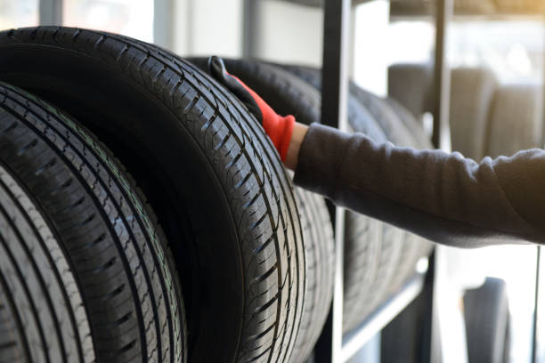 mecánico masculino sosteniendo el neumático mientras repara el fondo del garaje de servicio. - neumático fotografías e imágenes de stock