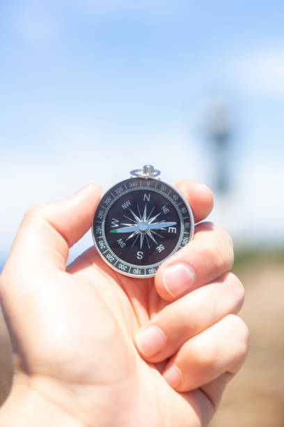 istock Hand holding a compass in front of a lighthouse on the coast. 1390680107