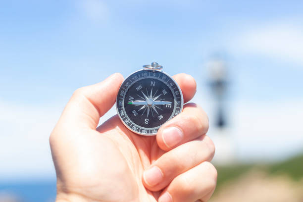 istock Hand holding a compass in front of a lighthouse on the coast. 1390680112