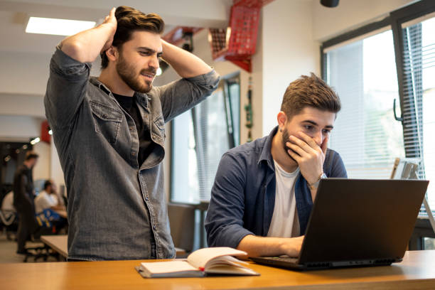Two worried men reading bad news on laptop in the office stock photo