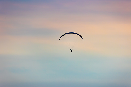 silhouette of a single paraglider in the distance against blurred pastel-coloured cloudy sky, Burg Hohenneuffen, Germany
