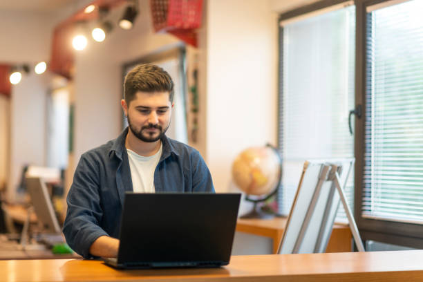 Happy young man using his laptop while sitting in the office stock photo