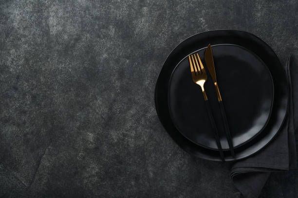 istock Ceramic empty black plate, silverware and linen kitchen towel napkin on old black ceramic cement concrete table background. Cooking stone backdrop. Top view with copy space. Flat lay 1390682651